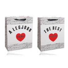 PAPIEROVÁ TAŠKA S MATNOU KLOPOU SO STUHOU, ČIERNY MEDZINÁRODNÝ NÁPIS NA BIELOM POZADÍ, "A LEGJOBB FÉRJ/ THE BEST HUSBAND" S ČERVENÝM SRDCOM