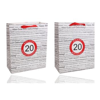 PAPIEROVÁ TAŠKA S MATNOU KLOPOU SO STUHOU, ČIERNA NA BIELOM POZADÍ, S NÁPISOM "HAPPY BIRTHDAY" V NIEKOĽKÝCH MEDZINÁRODNÝCH JAZYKOCH NA POZADÍ, ČERVENÝ KRÚŽOK S LETOPOČTOM "20"