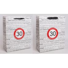 PAPIEROVÁ TAŠKA S MATNÝMI, STUŽKOVÝMI ZÁLOŽKAMI, ČIERNA NA BIELOM POZADÍ, S NÁPISOM "HAPPY BIRTHDAY" V NIEKOĽKÝCH MEDZINÁRODNÝCH JAZYKOCH NA POZADÍ, ČERVENÝ KRUH S LETOPOČTOM "30"