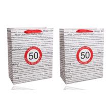 PAPIEROVÁ TAŠKA S MATNÝMI, STUŽKOVÝMI ZÁLOŽKAMI, ČIERNA NA BIELOM POZADÍ, S NÁPISOM "HAPPY BIRTHDAY" V NIEKOĽKÝCH MEDZINÁRODNÝCH JAZYKOCH NA POZADÍ, ČERVENÝ KRÚŽOK S ROKOM "50"